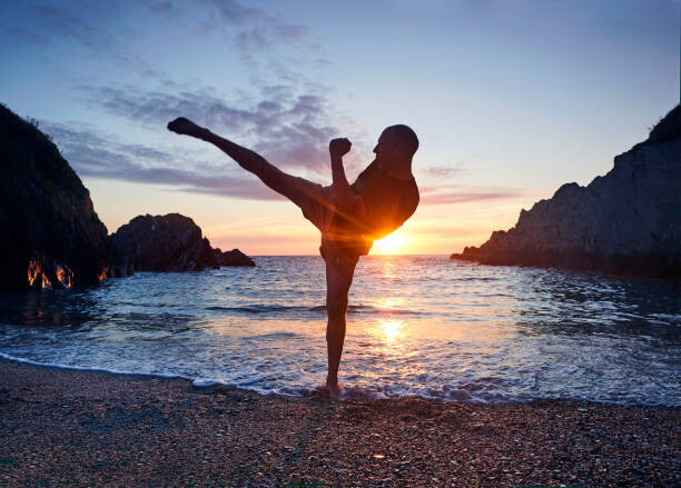Allan Baxter Umělecká fotografie Man practising kung fu kick along beach at sunset, Allan Baxter, (40 x 30 cm)