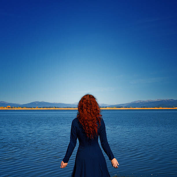 Anna Gorin Umělecká fotografie Redhead in blue dress faces rippled lake, Anna Gorin, (40 x 40 cm)