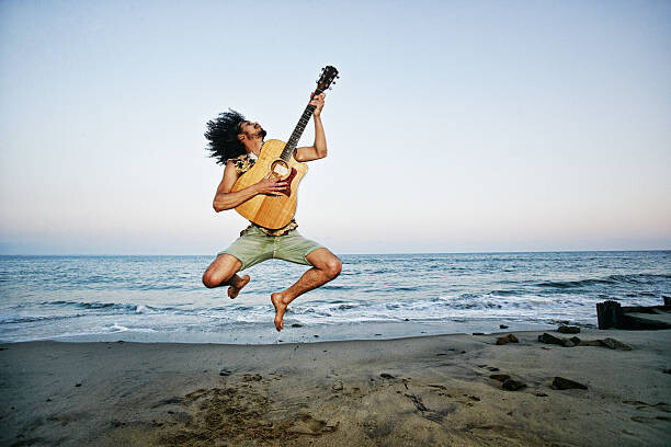 Peathegee Inc Umělecká fotografie Mixed Race man playing guitar and jumping at beach, Peathegee Inc, (40 x 26.7 cm)