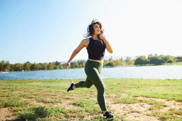The Good Brigade Plakát, Obraz - Smiling young woman jogging near lake on sunny day, The Good Brigade, 40 × 26.7 cm