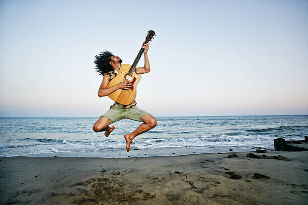 Peathegee Inc Plakát, Obraz - Mixed Race man playing guitar and jumping at beach, Peathegee Inc, 40 × 26.7 cm