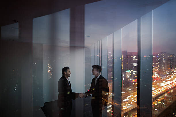 Shannon Fagan Plakát, Obraz - Businessmen shaking hands in office at night, Shannon Fagan, 40 × 26.7 cm